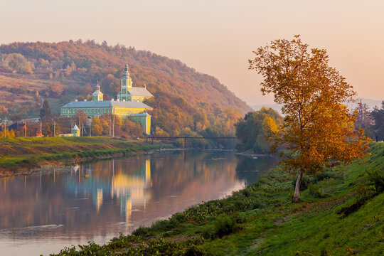 mukachevo, ukraine - 06 nov 2015: old town with latorica river in autumn. embankment with trees in fall season. saint nicholas monastery in the distance. urban scenery in morning light