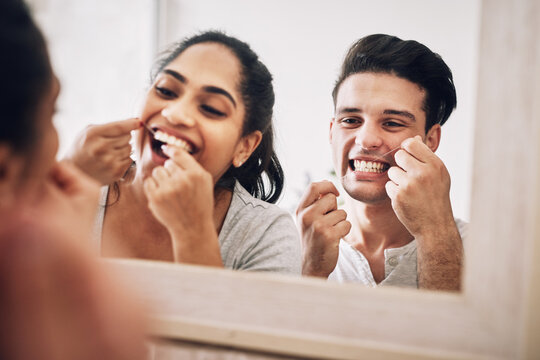 Couple, dental floss and mirror in bathroom, home and together for hygiene, process and routine in house. People, man and woman with reflection for benefits, excited and teeth whitening at apartment