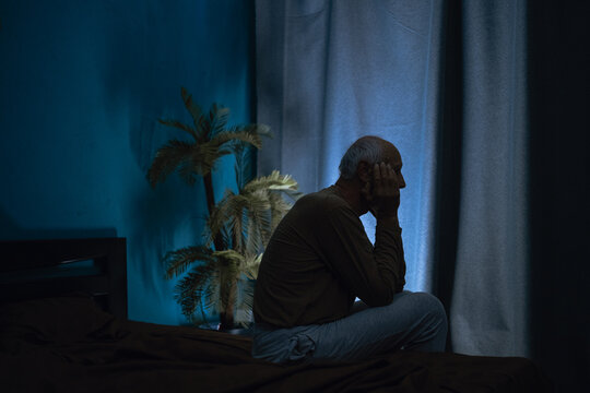 Silhouette of lonely old man suffering from depression in bedroom, pensioner suffering from insomnia sitting on bed at night sleepy.