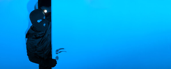 A cloaked individual cautiously opens a blue door in a darkened environment, illuminating the space...