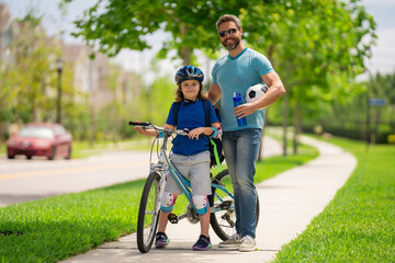 Obraz premium Father and son in bike helmet learning ride bicycle. Father and son on bicycle on summer day outdoor. Little son trying to ride bicycle with father. Fathers day. Childhood and fatherhood. Child care.