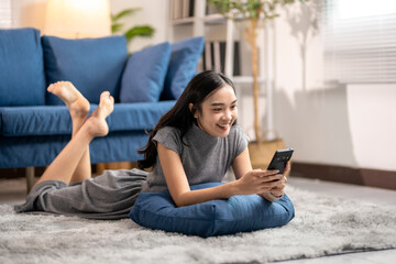 Obraz premium Happy young woman relaxing on floor at home using smartphone