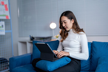 Young asian businesswoman sitting on sofa and using digital tablet with keyboard