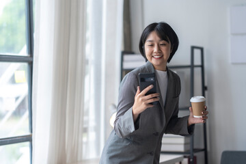 Businesswoman holding coffee and using smartphone in modern office