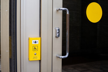 Button for calling staff help for people with disabilities. Wheelchair sign next to the button for assistance at the entrance of building on door