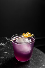An alcoholic cocktail in a lowball rocks glass served with ice sphere garnished with a lollypop