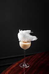 An alcoholic cocktail served straight up in coupe glass with cotton candy garnish