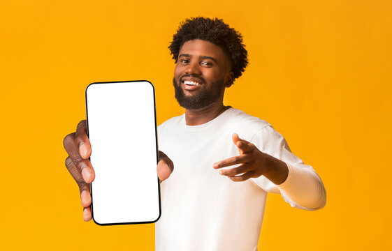 Cheerful black guy indicating happily at camera, greeting someone, orange studio background
