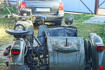 one old iron broken dirty rusty retro powerful with sidecar green heavy industrial motorcycle stands on the ground near the black car in the daytime on the street