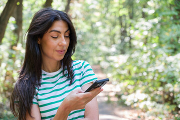 Portrait of beautiful young woman looking her phone in the city park 