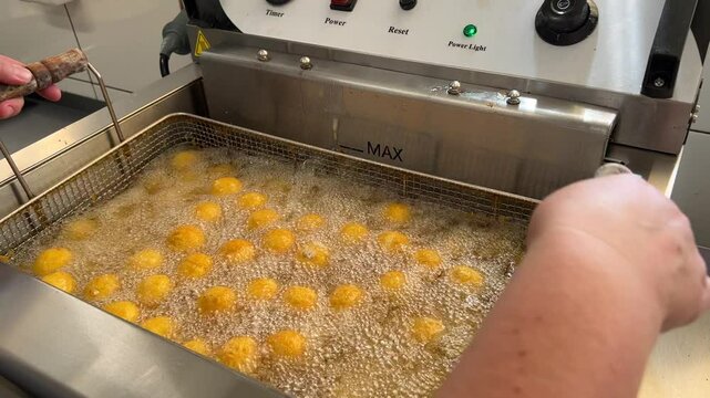 close-up in a professional kitchen, frying mozzarella cheese balls in oil in a deep fryer