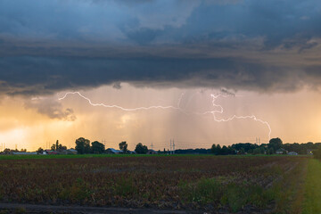 Lightning bolts below the base of an autumn thunderstorm at sunset