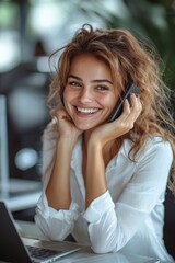 Fototapeta premium Confident businesswoman in a white blouse smiling while talking on the phone at her desk in a modern office environment