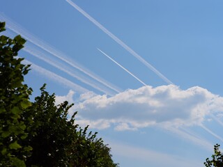 Obraz premium Airplane condensation trails (contrails) in the blue sky going out of a cloud
