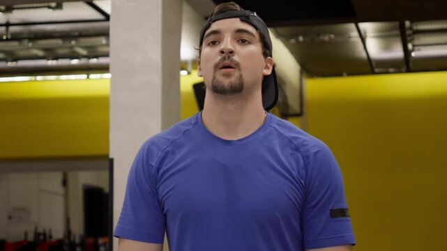 Man Performing Upright Row with Barbell in the Gym. Man in a cap and blue shirt executing an upright row with a barbell, ideal for strength training and fitness content.