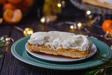 Cut Christmas mini tart with mandarin filling and cream on green plate on dark wooden background. Holiday desserts.