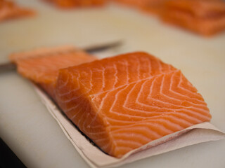 A pristine piece of salmon is carefully placed on a kitchen board, its delicate layers glistening under the light. The salmon's vibrant color highlights its freshness and quality.