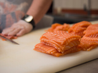 A Japanese cuisine master carefully slices fresh salmon into perfect portions. The special knife ensures each cut of salmon is even, while the chef's gloved hands highlight the precision of his work.
