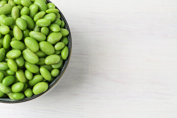 Fresh edamame soybeans in bowl on white wooden table, top view. Space for text