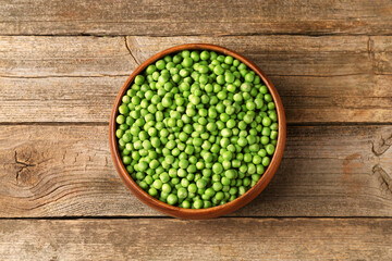 Fresh green peas in bowl on wooden table, top view