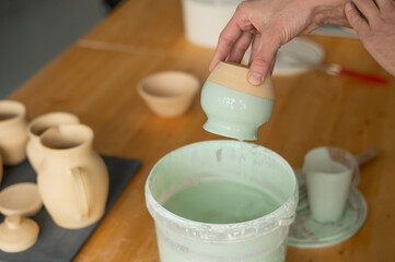 Close-up of a potter's hands glazing a pottery piece. 