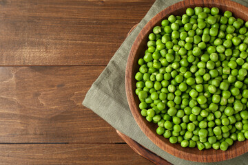 Fresh green peas in bowl on wooden table, top view. Space for text