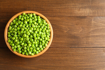 Fresh green peas in bowl on wooden table, top view. Space for text