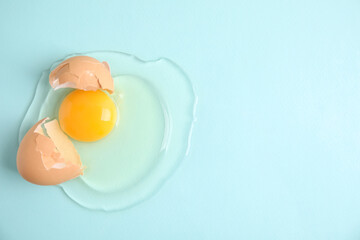 Broken raw egg with shell on light blue background, top view. Space for text