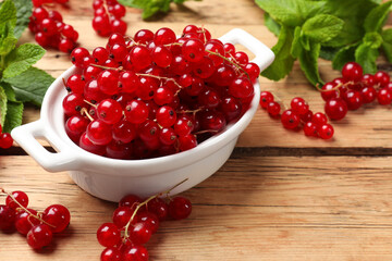 Fresh red currants in bowl and mint on wooden table, closeup