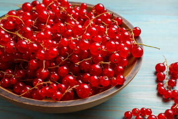 Fresh red currants in bowl on light blue wooden table, closeup