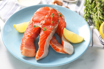 Plate with fresh salmon steaks, lemon and thyme on white marble table, closeup