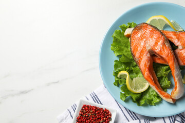 Tasty grilled salmon steaks, lettuce, lemon and spices on white marble table, flat lay. Space for text