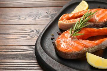 Tasty grilled salmon steaks, lemon and spices on wooden table, closeup. Space for text