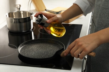 Woman with bottle of oil and frying pan in kitchen, closeup
