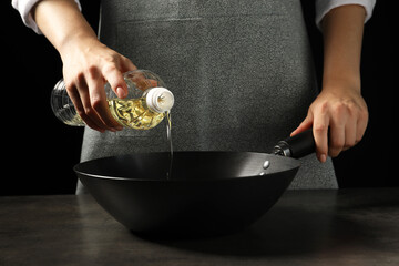 Woman pouring oil into frying pan at gray textured table, closeup