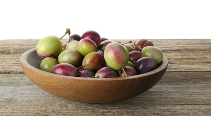 Many ripe plums in bowl on wooden table against white background