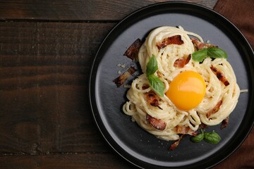 Delicious pasta Carbonara with egg yolk, bacon and basil on wooden table, top view. Space for text