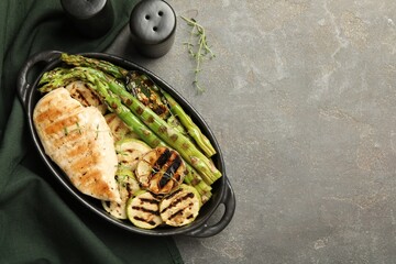 Delicious grilled vegetables and chicken breast in baking dish on grey table, flat lay. Space for text