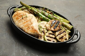 Delicious grilled vegetables and chicken breast in baking dish on grey table, closeup