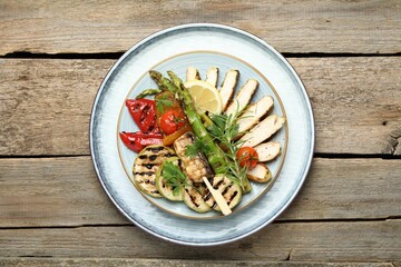 Delicious grilled vegetables and cut chicken meat on wooden table, top view