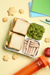 Lunch box with snacks, bottle and stationery on yellow table, flat lay