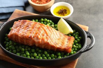 Delicious grilled salmon fillet with green peas and lime in baking dish on grey table, closeup