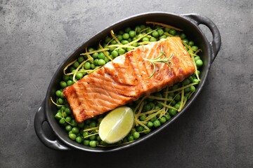 Delicious grilled salmon fillet with green peas and lime in baking dish on grey textured table, top view