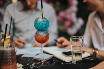 Vibrant cocktails served during an outdoor business meeting. Colleagues engaged in conversation and note-taking, creating a lively and creative work environment.