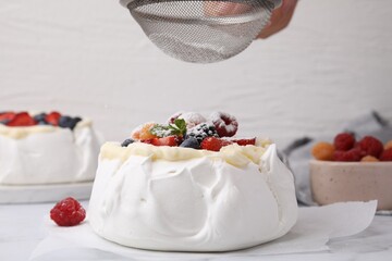 Woman sprinkling powdered sugar onto Pavlova cake (meringue dessert) at table, closeup