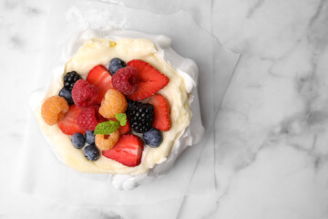 Pavlova cake (meringue dessert) with whipped cream, fresh berries and mint on white marble table, top view. Space for text