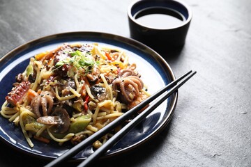 Stir-fry noodles with sea food, vegetables and soy sauce on dark textured table, closeup