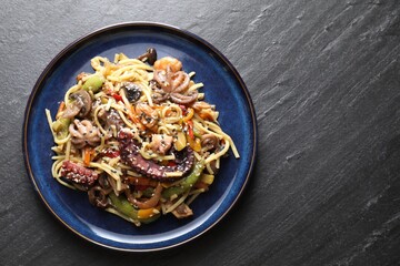 Stir-fry noodles with sea food and vegetables on dark textured table, top view. Space for text