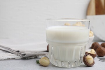 Glass of macadamia milk and nuts on white table, closeup