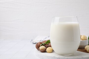 Glass of macadamia milk and nuts on white tiled table, closeup. Space for text